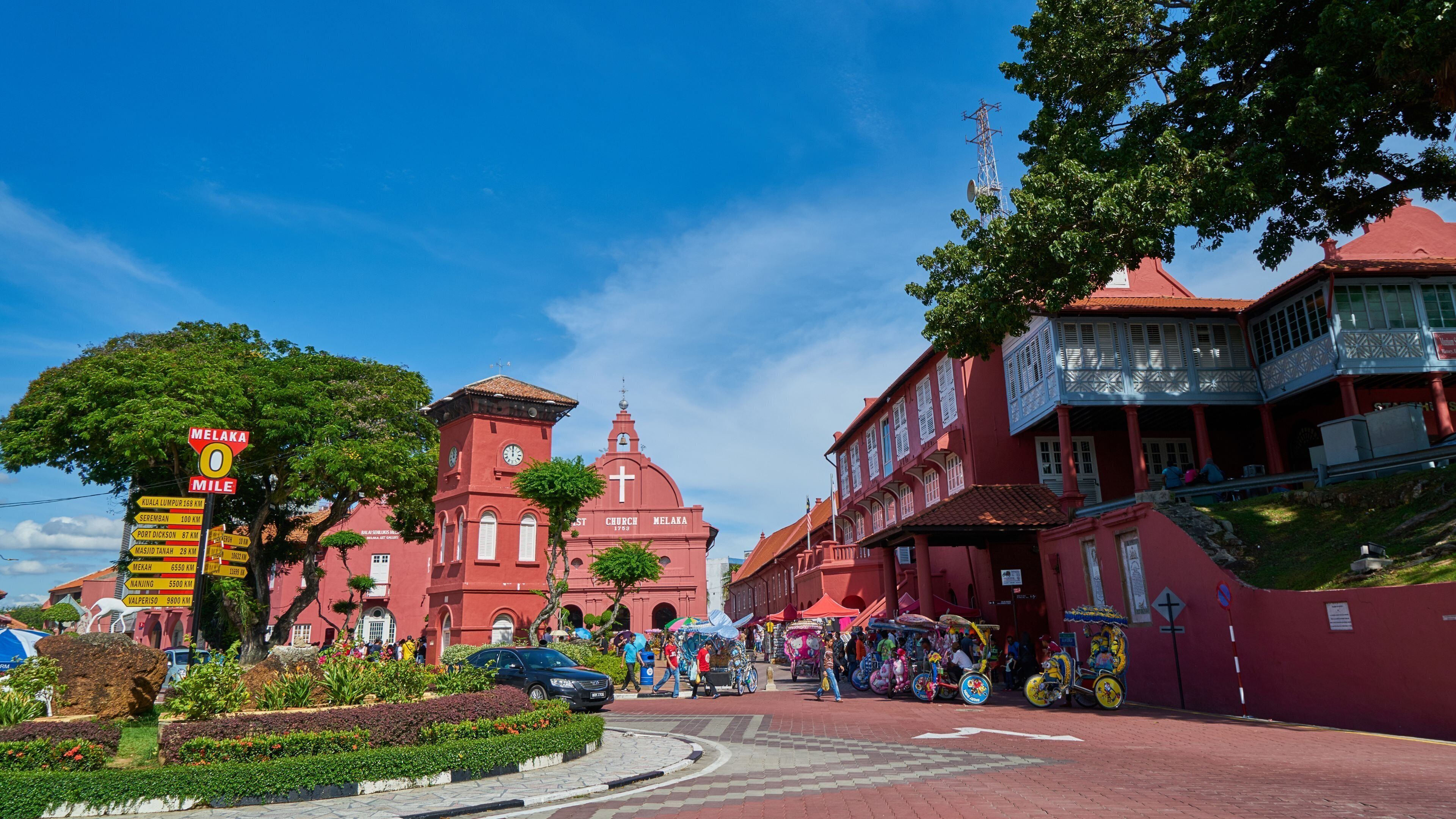 A red church with a clock tower, surrounded by a market area with colorful decorations and people.