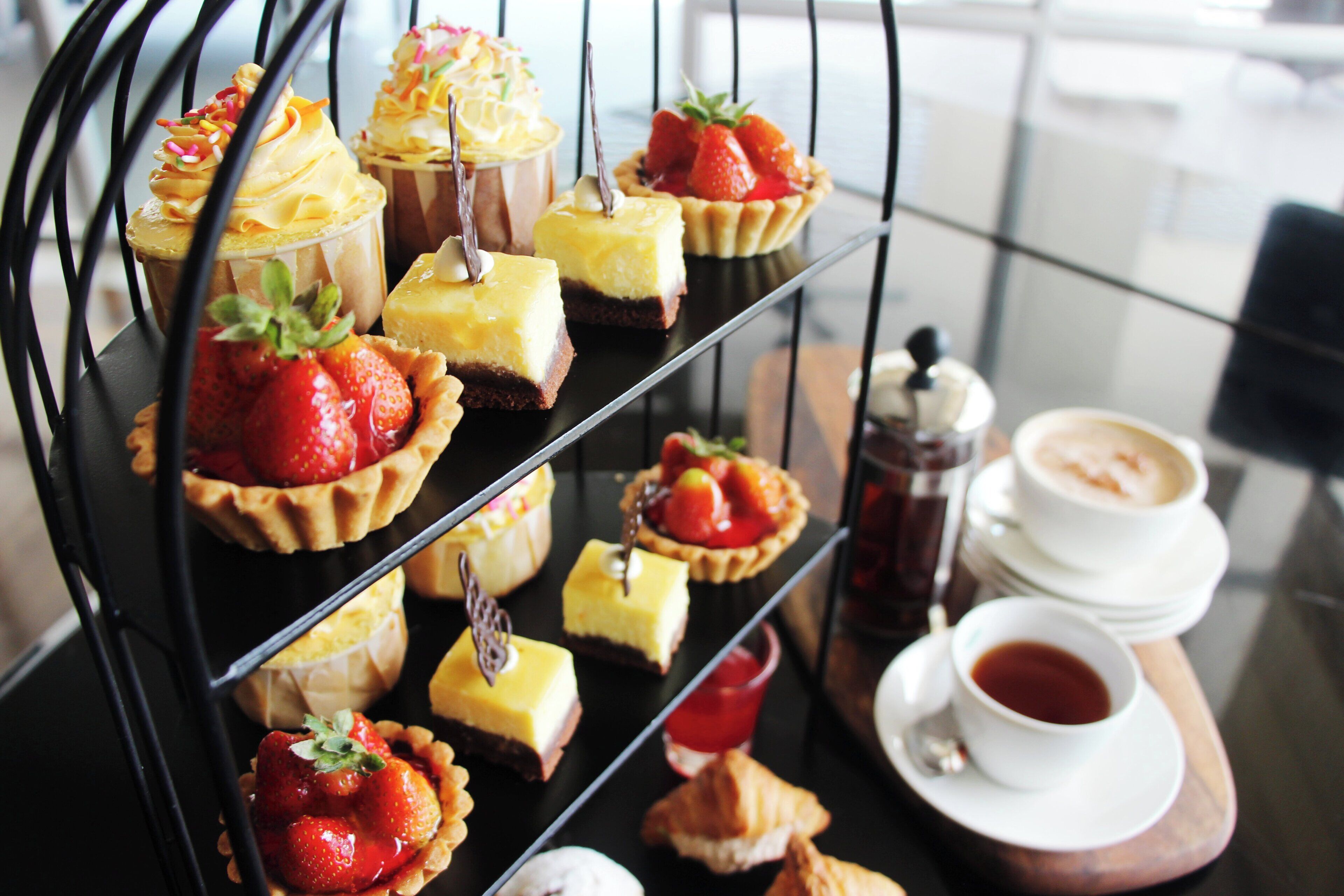 A dessert display with various cakes and pastries, including strawberry-topped tarts and a tray of coffee and tea.