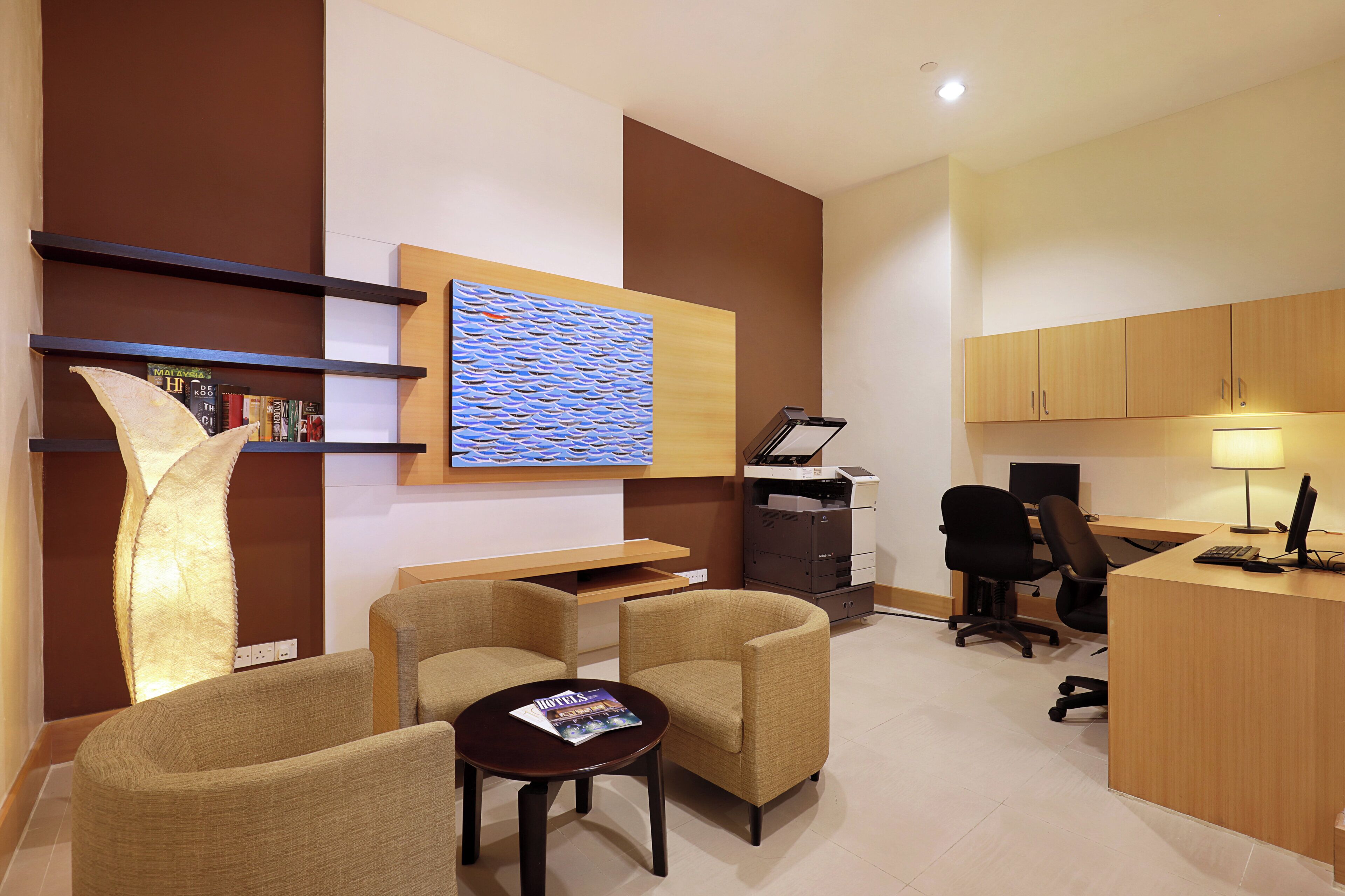 A modern office space with a desk, two chairs, a bookshelf, a printer, and a wall-mounted artwork.