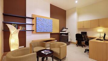 A modern office space with a desk, two chairs, a bookshelf, a printer, and a wall-mounted artwork.