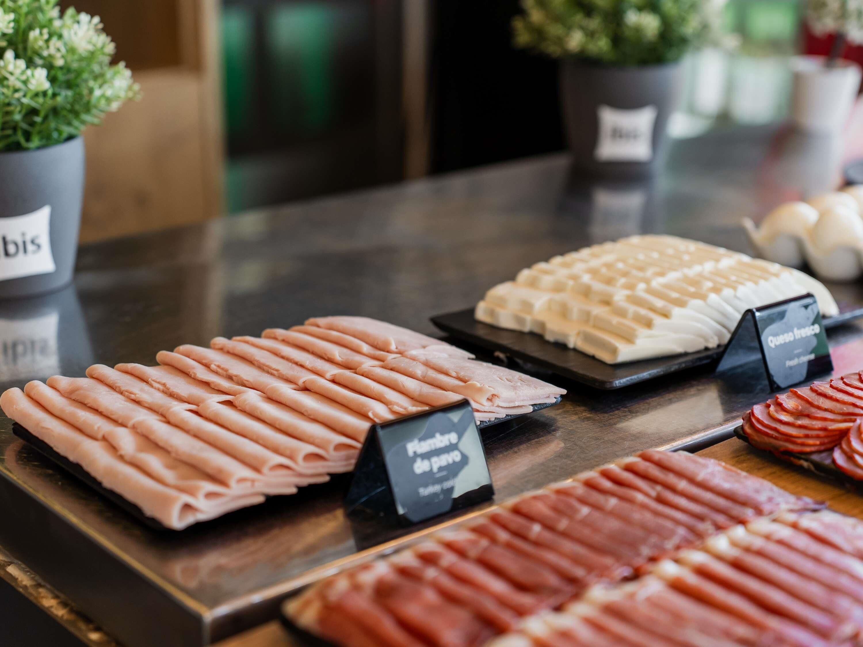 A variety of sliced meats on display, including ham and prosciutto, with labels indicating their names.