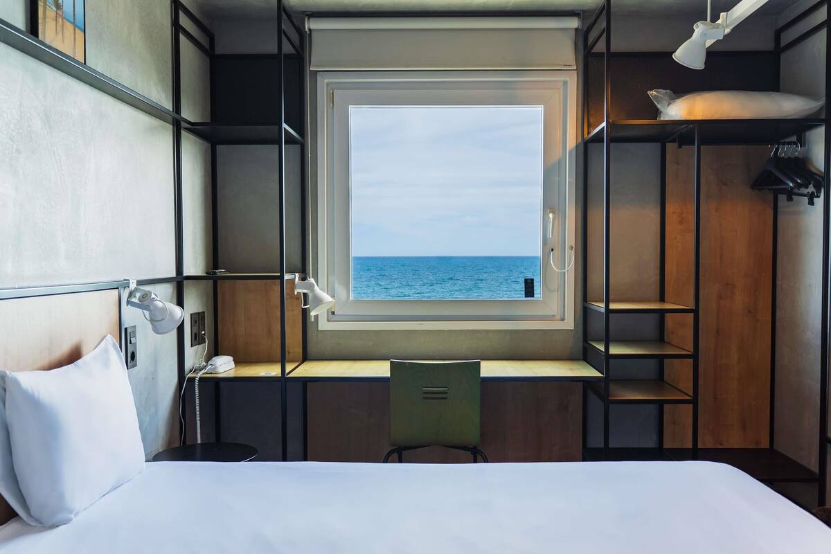 Una habitación compacta con cama, escritorio y ventana con vista al mar.