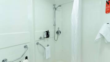 Ducha con cabezal de ducha de mano, mampara de vidrio, toallero y barra de apoyo.