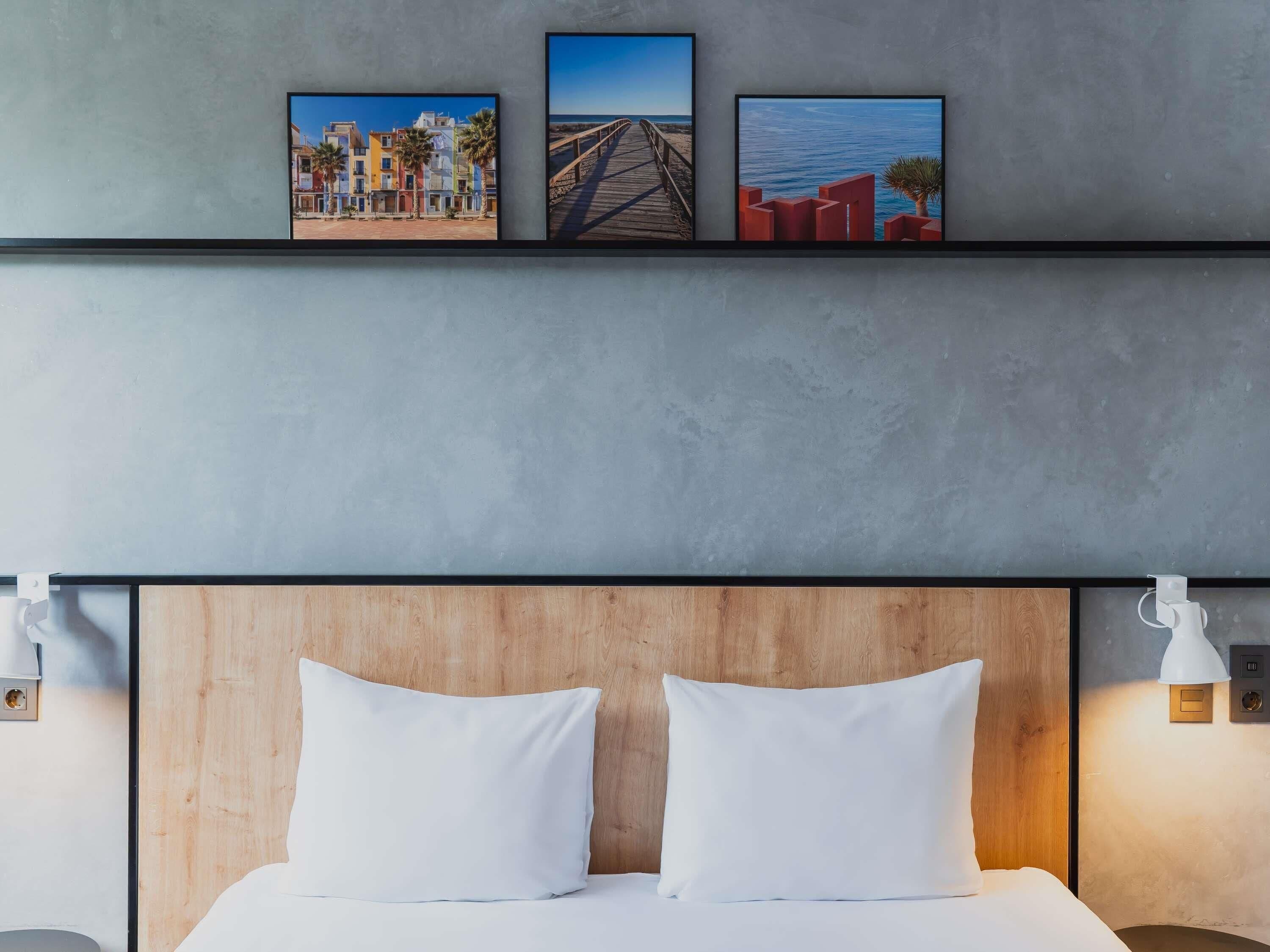 A hotel room with a wooden headboard, two white pillows, a bed, and three framed pictures on the wall.