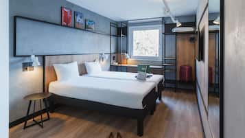 A modern hotel room with a large bed, bedside tables, a desk, and a window.