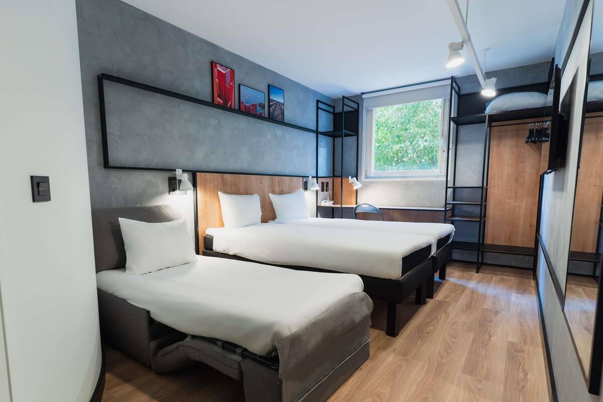Una habitación de hotel moderna con dos camas, un ventanal con vistas y suelo de madera.