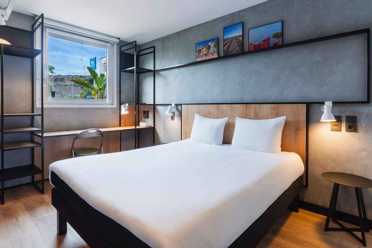 Una habitación de hotel moderna con una cama grande, un escritorio con una silla, una ventana con vistas y una obra de arte en la pared.
