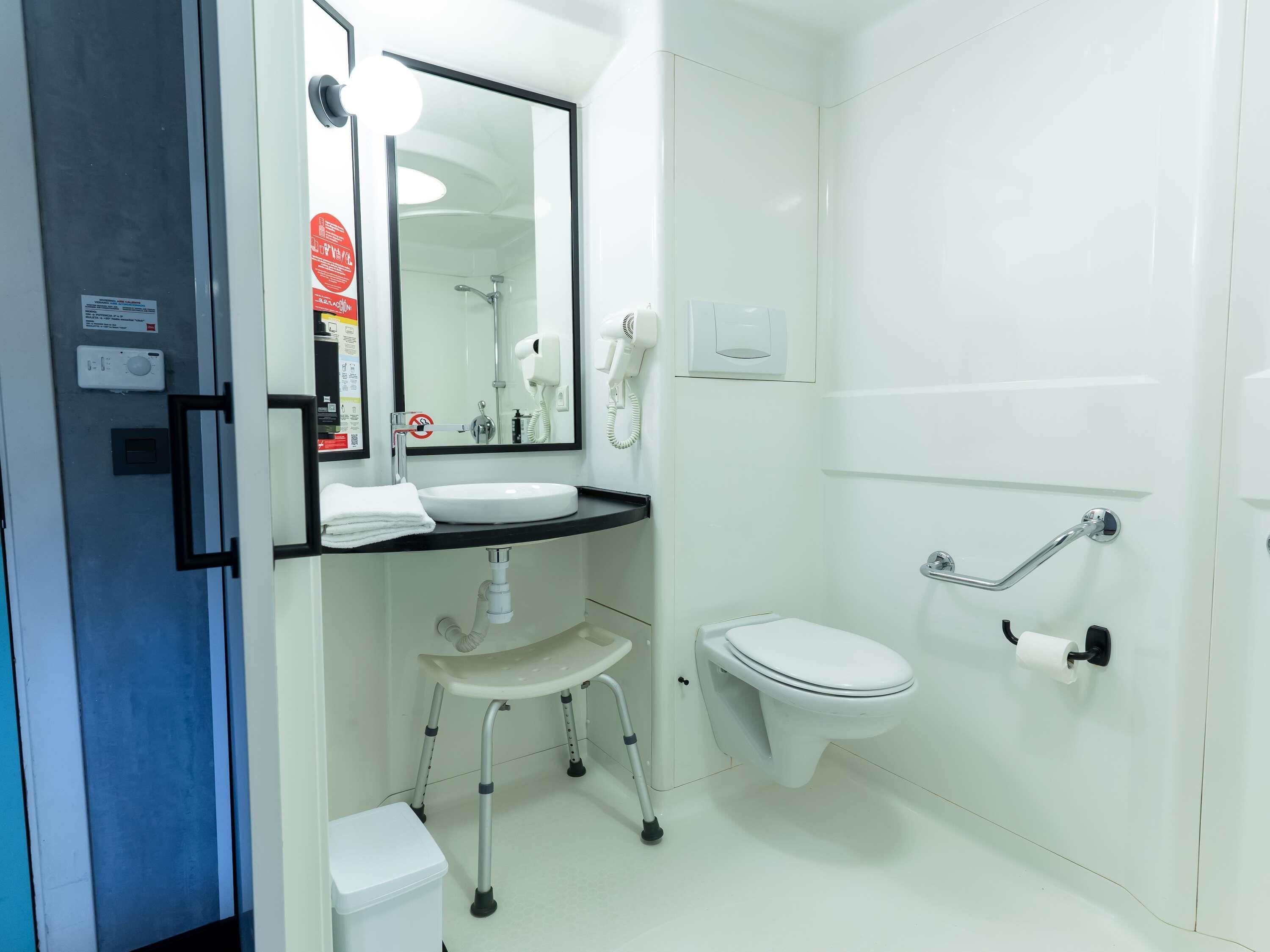 Un baño con lavamanos blanco, espejo, inodoro, zona de ducha y barandilla.