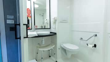 Un baño con lavamanos blanco, espejo, inodoro, zona de ducha y barandilla.