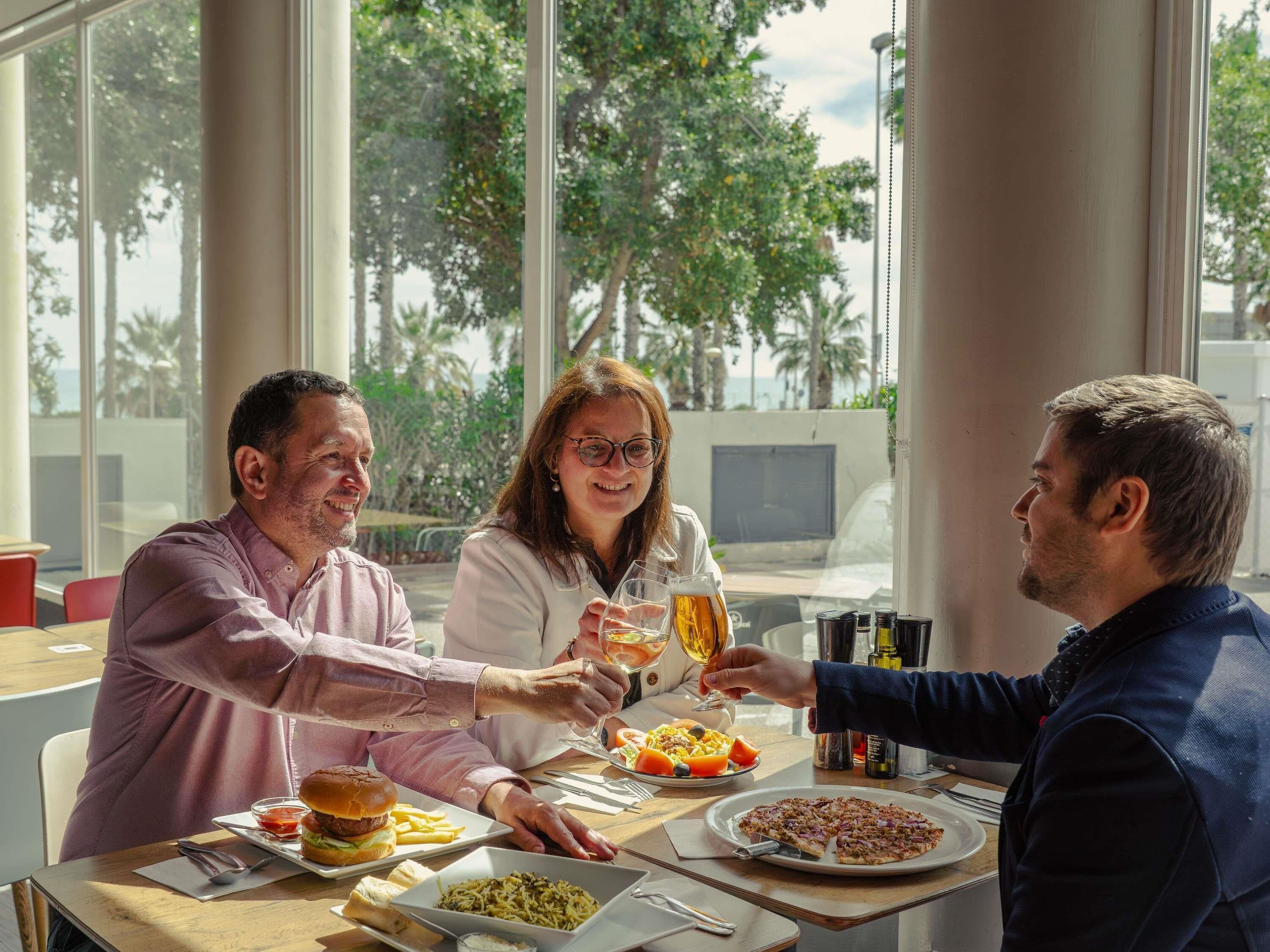 A group of people dining at a table with food and drinks.