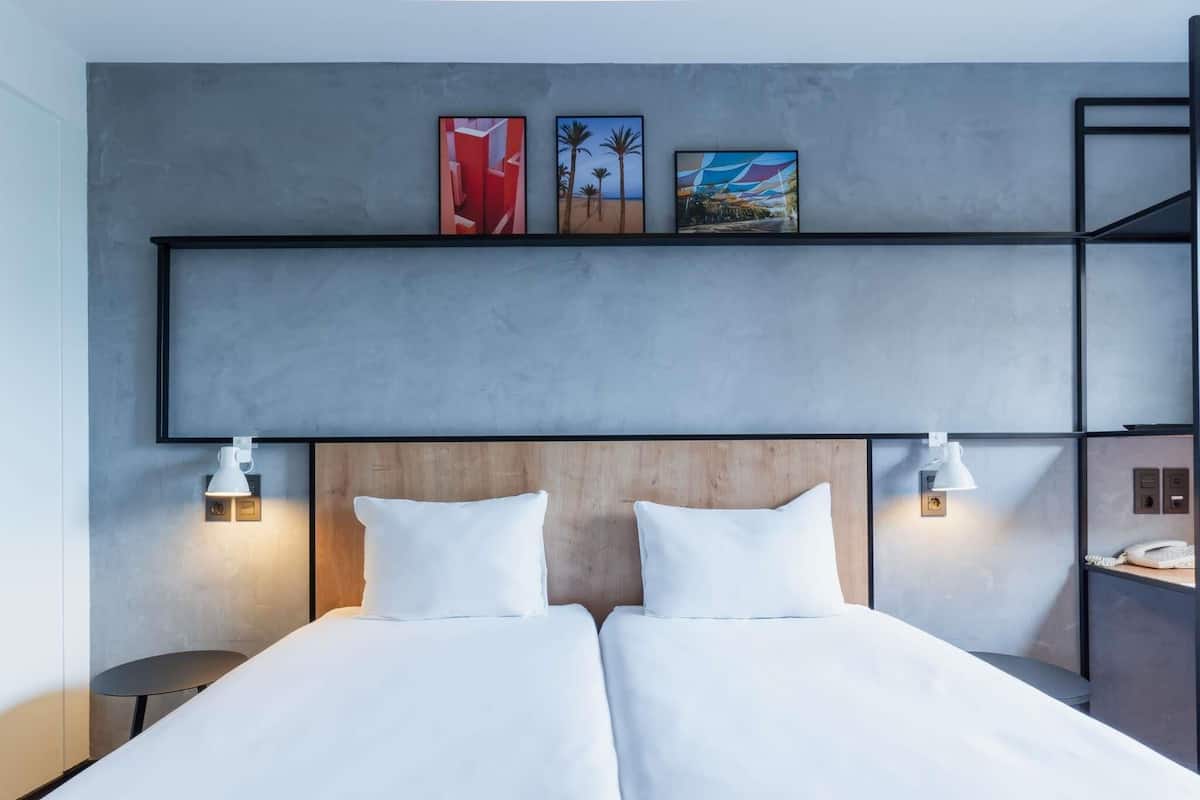 A double bed with white linens, two bedside lamps, a wooden headboard, and three framed artworks on the wall above.