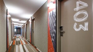 Un pasillo de hotel con alfombra estampada, puertas con un logotipo y una pared con textura.