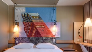 Habitación de hotel con cama, escritorio, silla y un amplio mural en la pared.