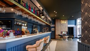 Una zona de bar con mostrador, taburetes y una variedad de botellas y vasos.