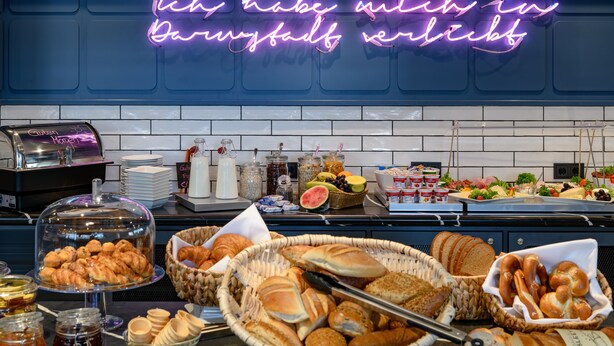 Un bufé de desayuno con panes, bollería y frutas variadas.