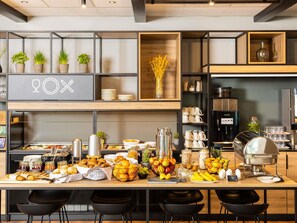 A buffet setup with various food items, a coffee machine, and a wine glass display. - ibis Dortmund City (Dortmund)