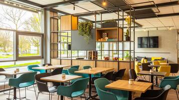 A modern cafe interior with wooden tables, teal chairs, and a large window offering a view of the street.