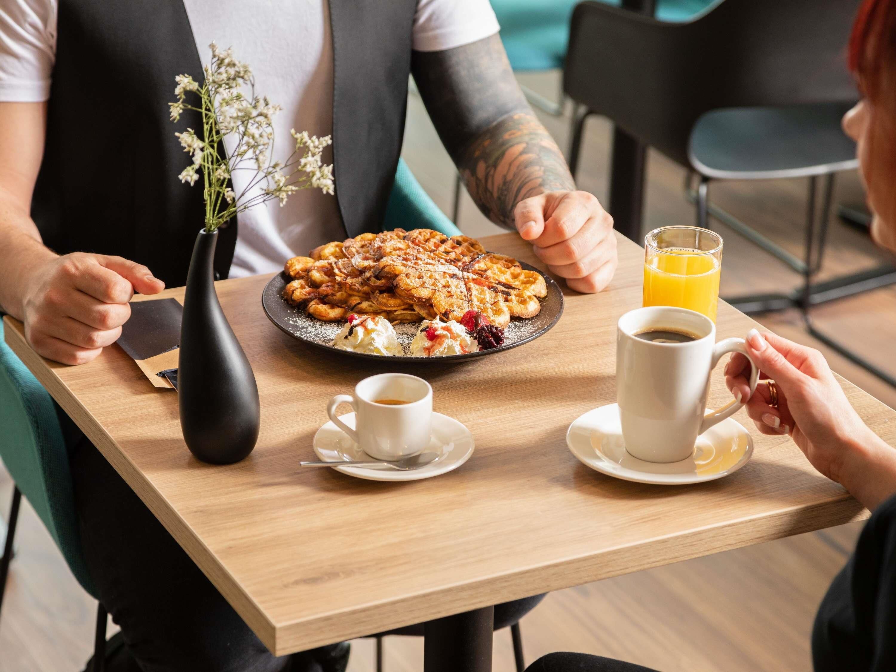 Ein Esstisch mit einer Platte Waffeln, zwei Kaffeetassen und einem Glas Orangensaft.