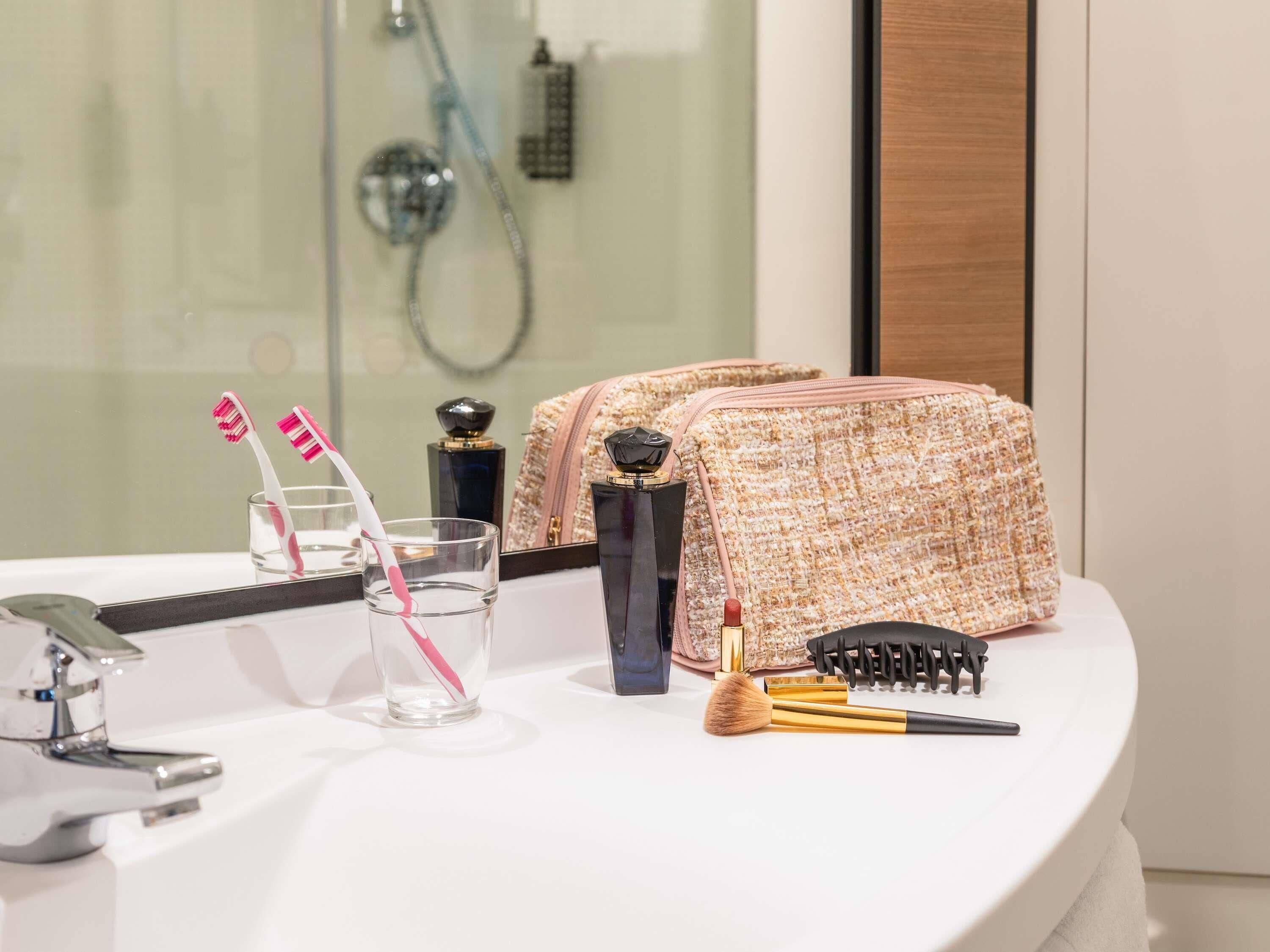Un baño con cabina de ducha de vidrio, un lavamanos blanco, un espejo y una bolsa de artículos de aseo sobre el mostrador.