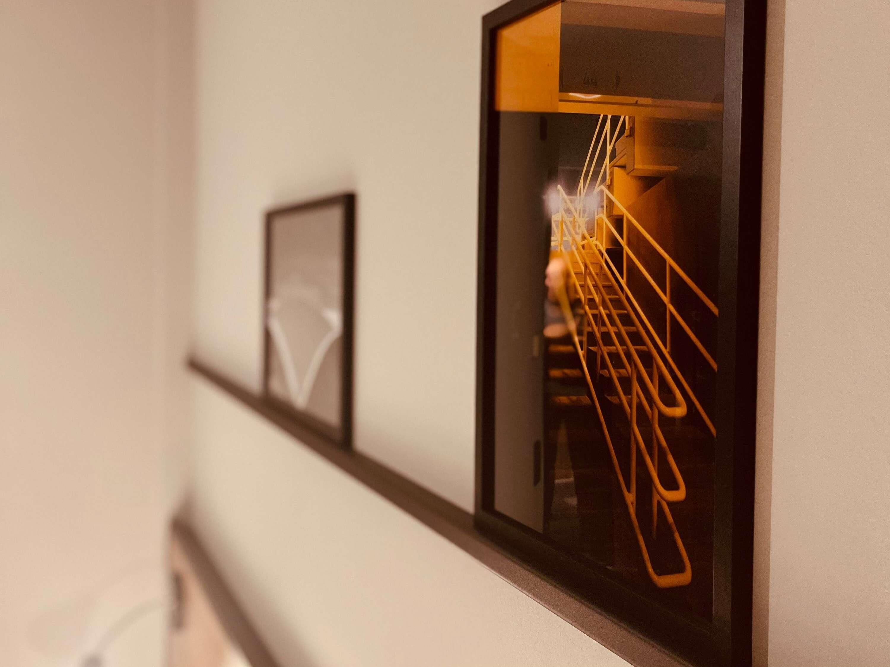 Un couloir orné de tableaux encadrés et une fenêtre donnant sur un escalier.