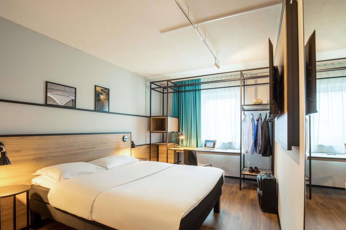 A hotel room with a large bed, a desk with a laptop, a TV, and a wardrobe.
