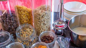 A variety of food items in glass containers, including granola, dried fruits, and nuts, with a bowl of yogurt and a spoon nearby.