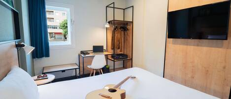 Una habitación de hotel con una cama, un escritorio con una computadora portátil, una guitarra y auriculares.