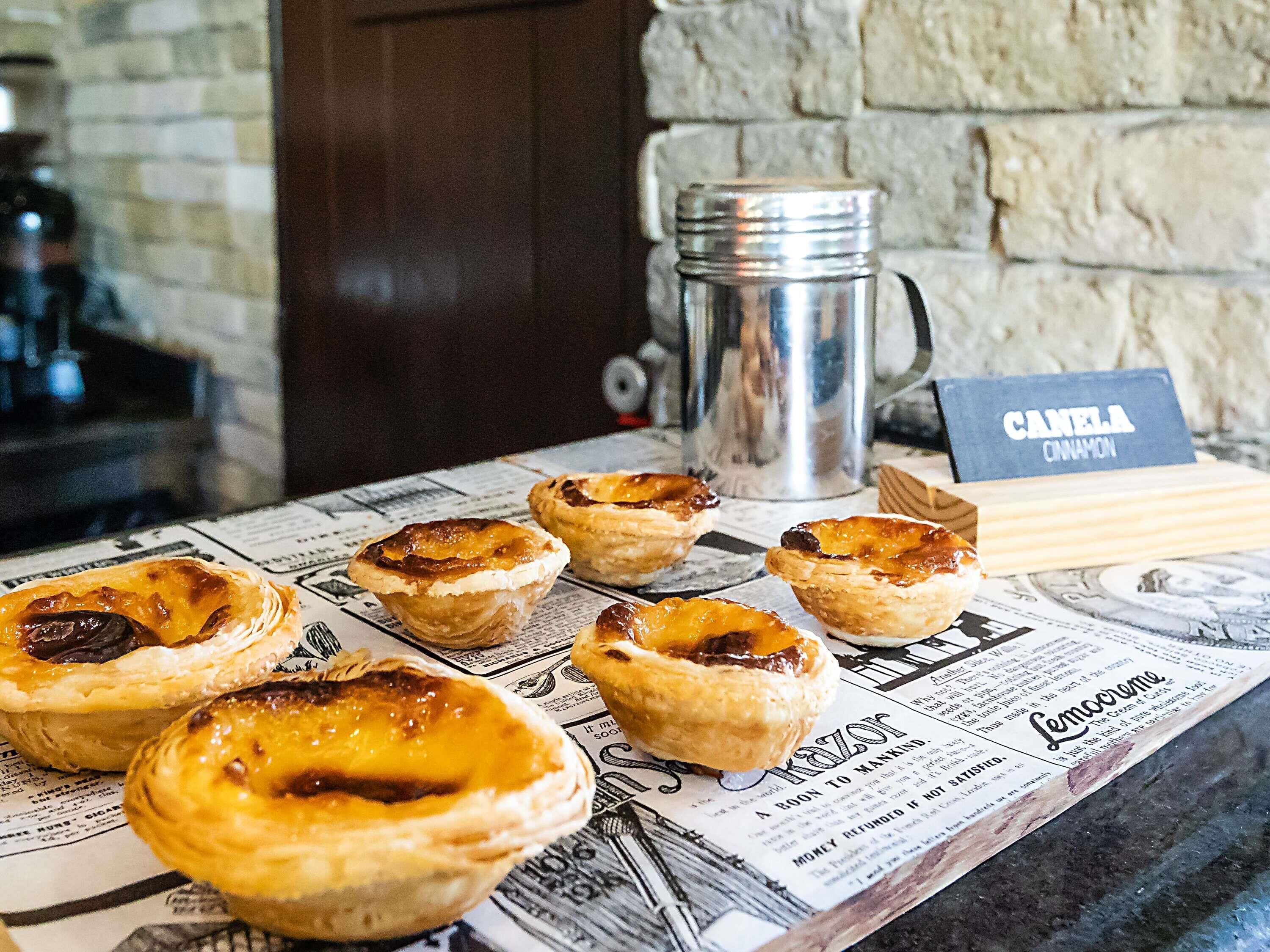 A table with several small pastries, a metal pitcher, and a menu with a 'CANELA CINNAMON' sign.