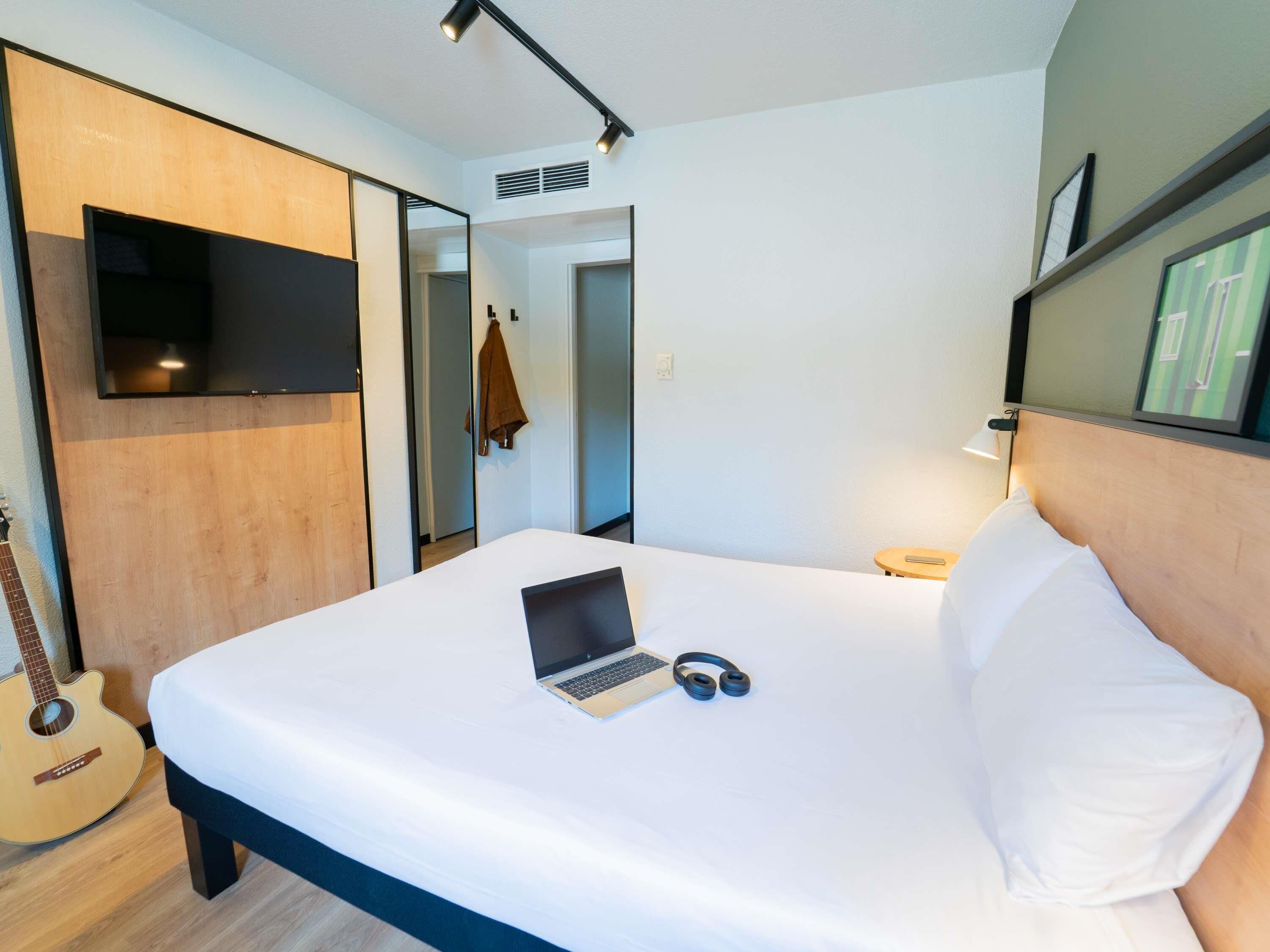 A bedroom with a bed, a laptop, headphones, and a guitar.