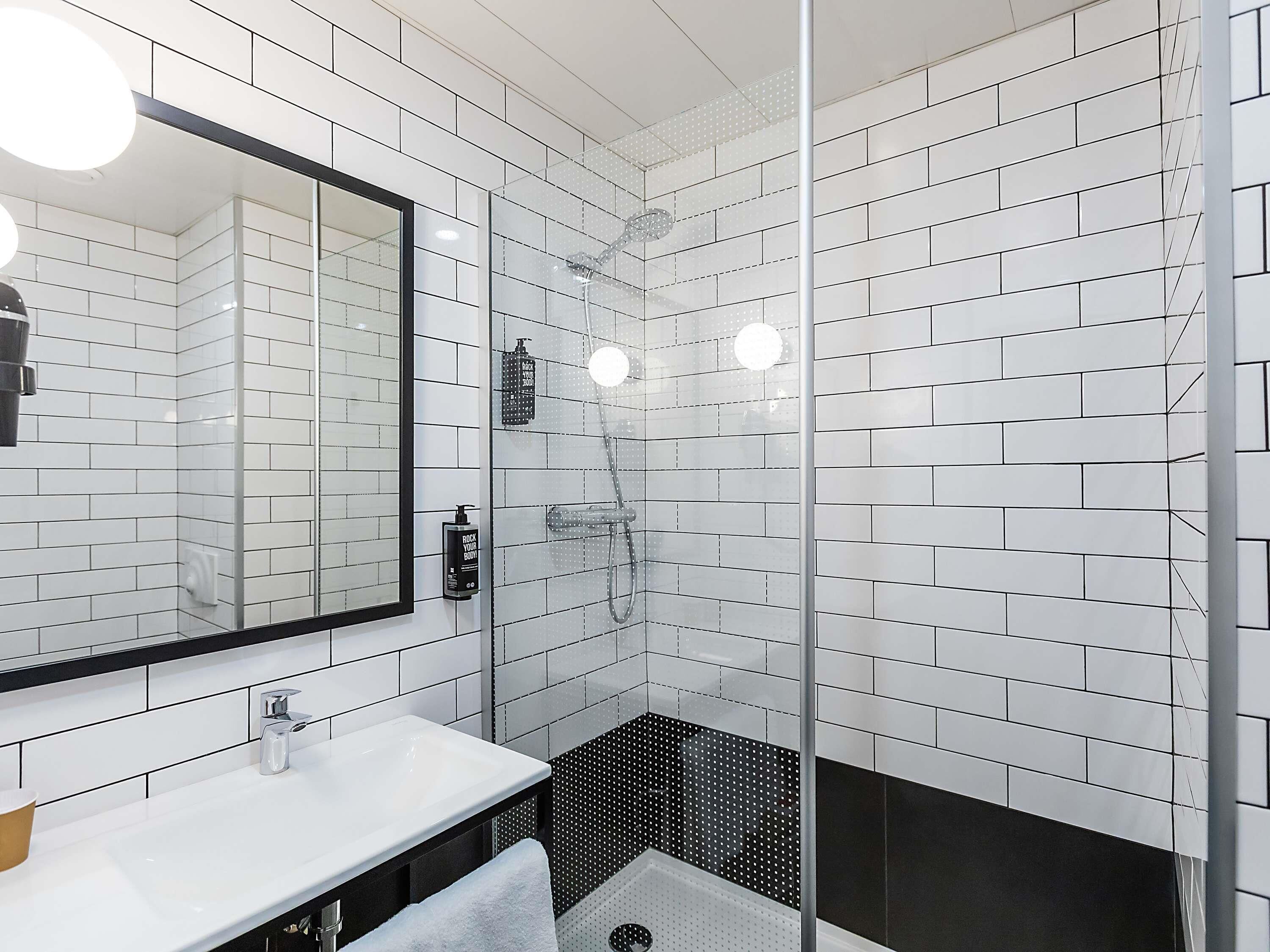 A modern bathroom with white subway tiles, a glass shower enclosure, a white sink, and a black and white tiled shower floor.