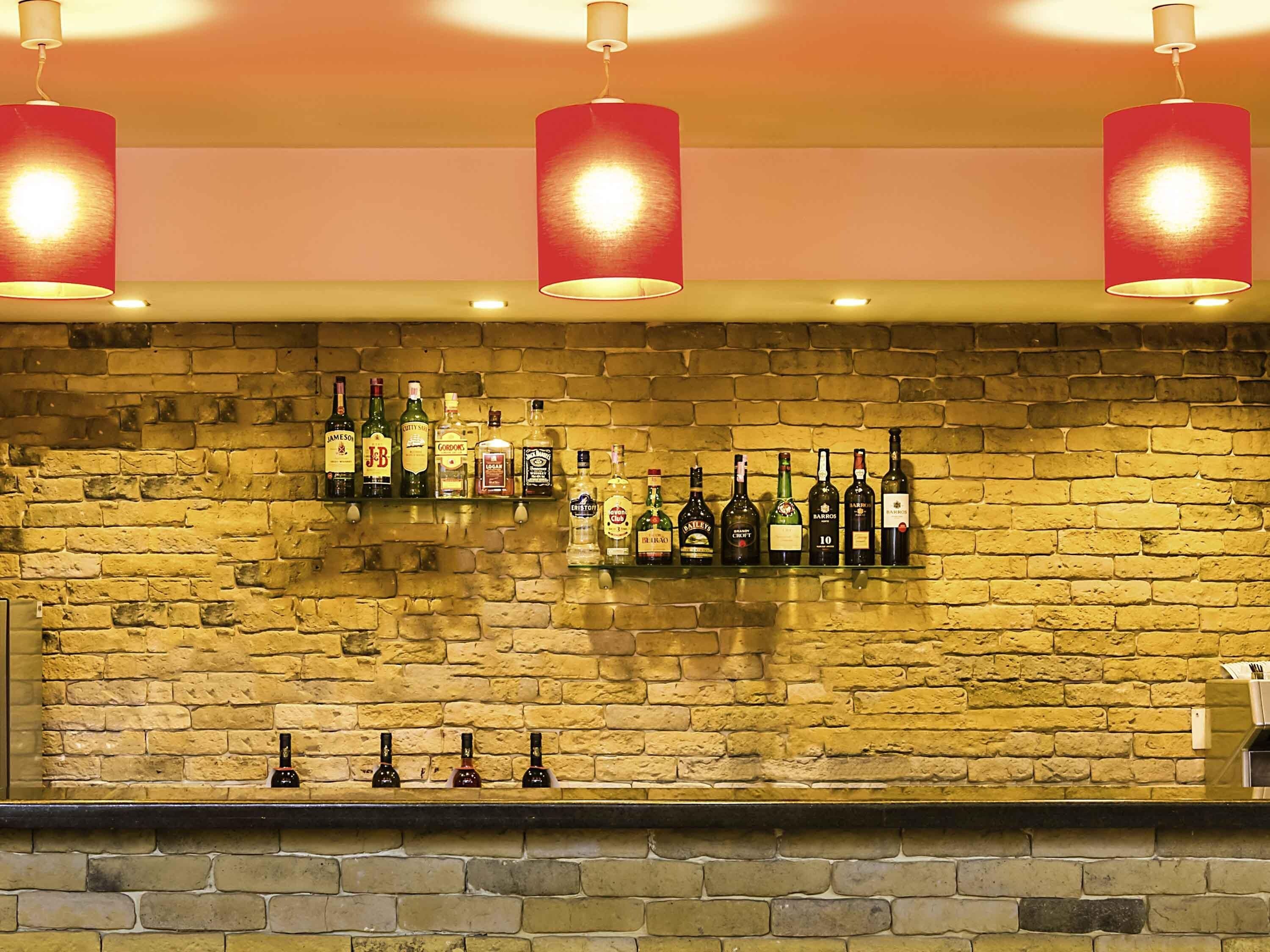 Zona de bar con pared de ladrillo, varias botellas de licor y lámparas colgantes rojas.