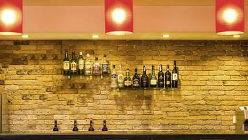 Zona de bar con pared de ladrillo, varias botellas de licor y lámparas colgantes rojas.