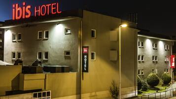 Een hotel met een opvallend “ibis HOTEL” bord, meerdere ramen en een goed verlichte gevel.