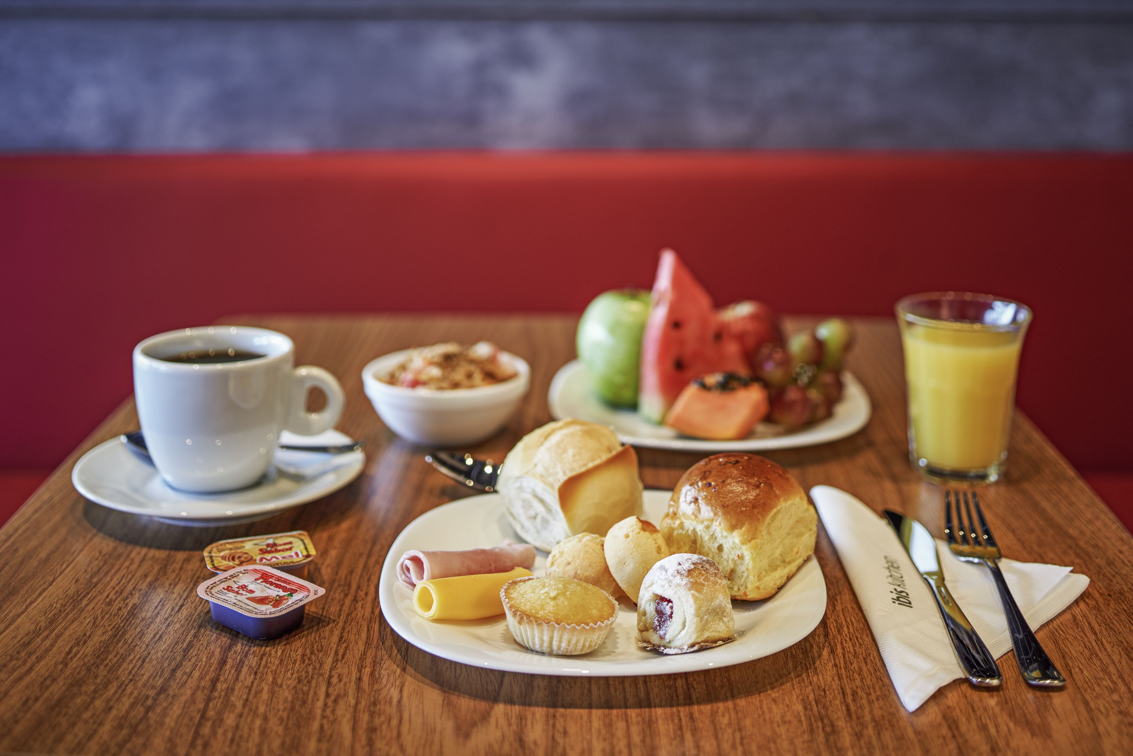 Ein Esstisch mit einer Kaffeetasse, einer Schüssel Müsli, einem Teller mit Gebäck, einem Glas Orangensaft und einem Teller mit Obst.