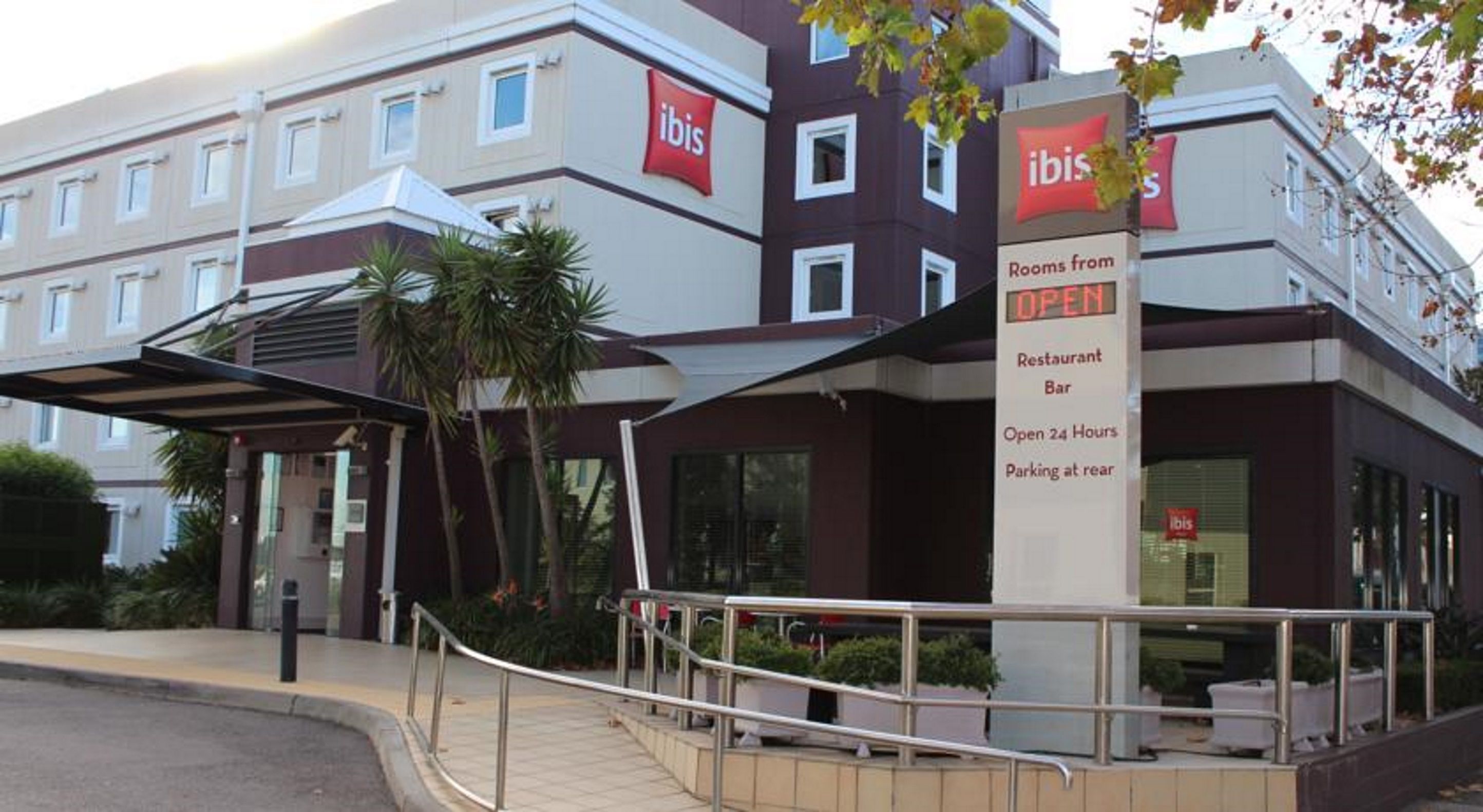 A hotel with an 'ibis' sign, indicating rooms from 'OPEN'. It has a restaurant/bar, open 24 hours, and parking at the rear.