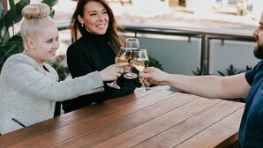 Una mesa de madera con tres personas brindando con copas de vino.