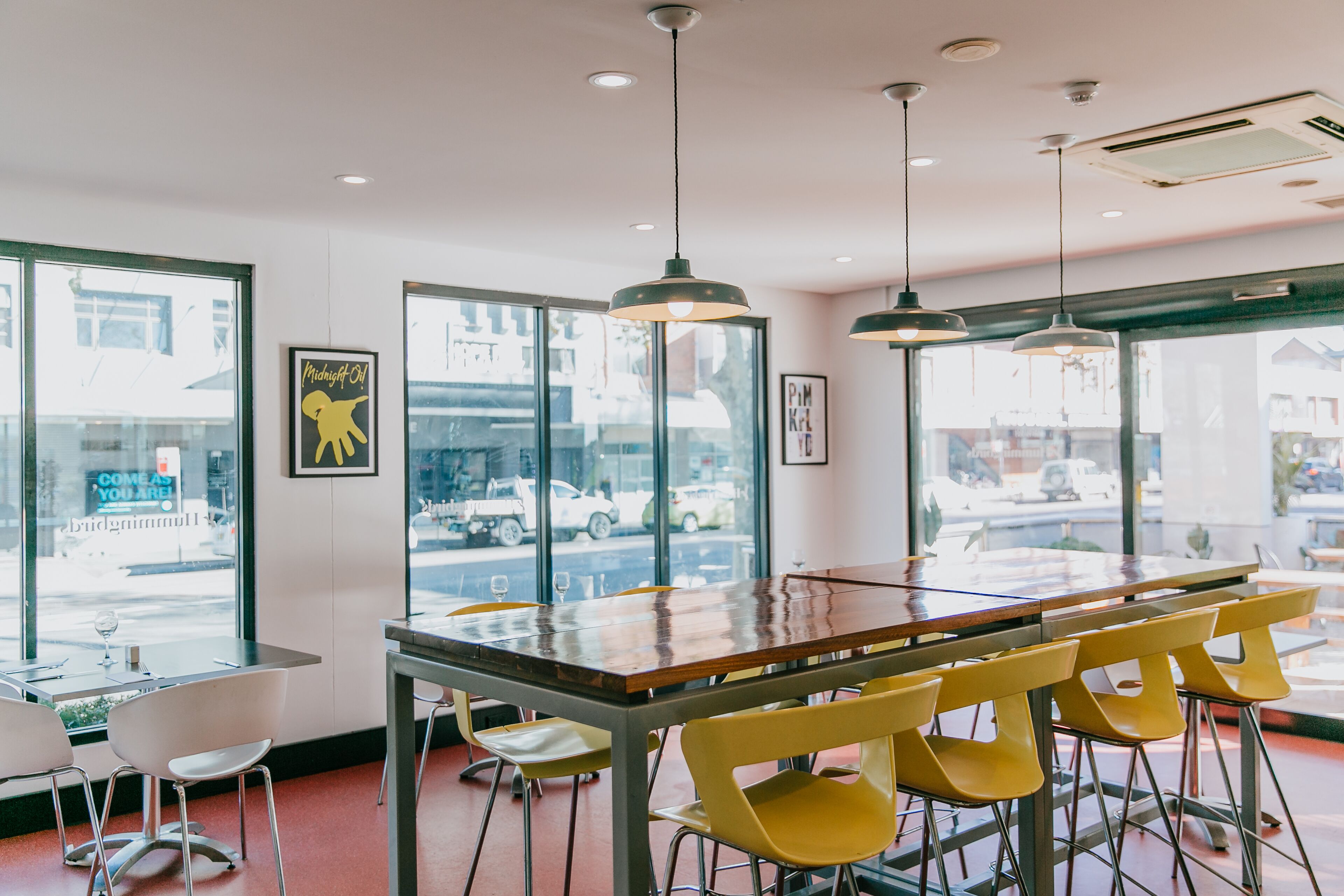Un restaurante con mesa de madera, sillas amarillas y lámparas colgantes.