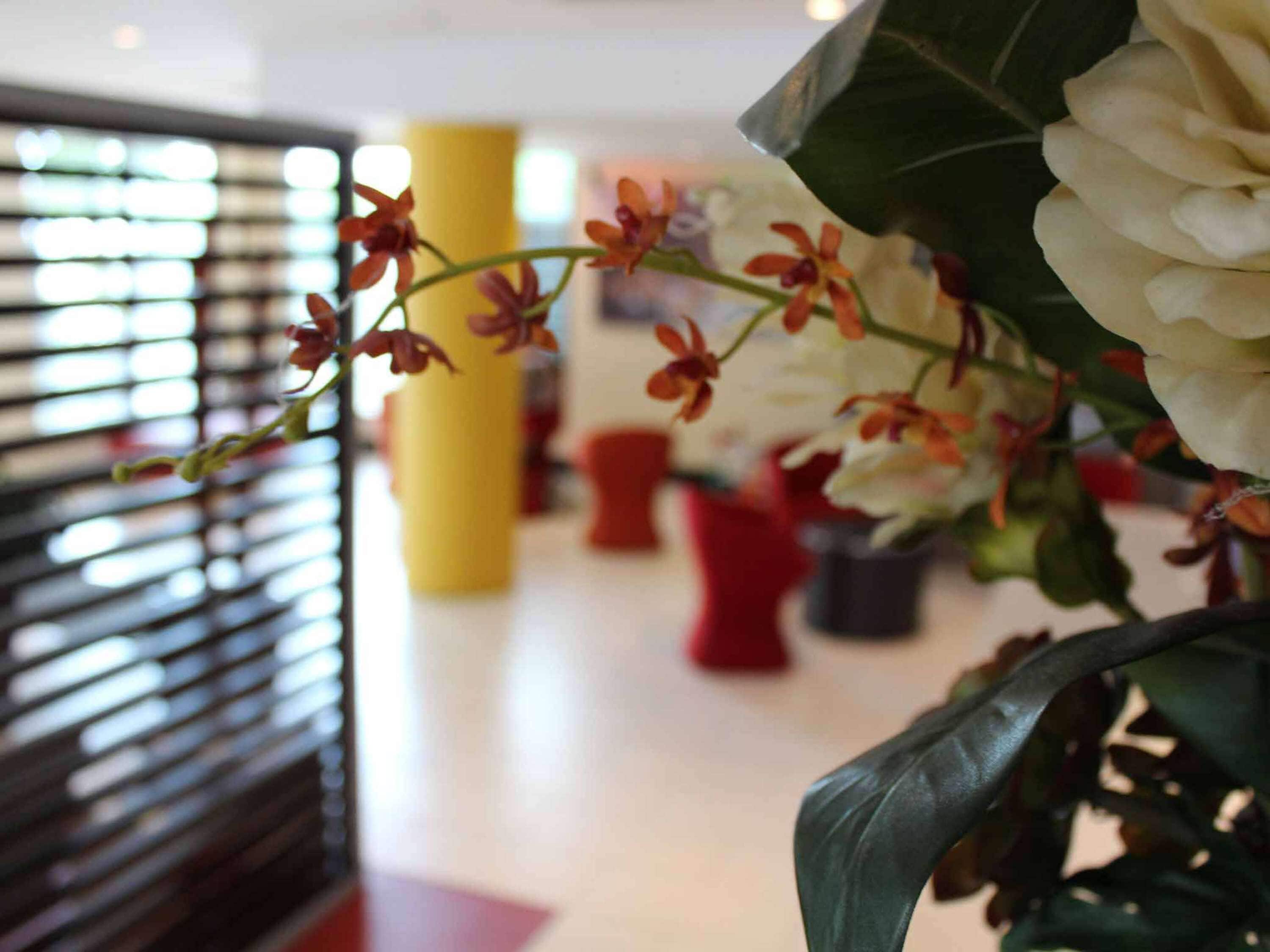 A hallway with a plant with white flowers and red buds, a yellow pillar, and red chairs.