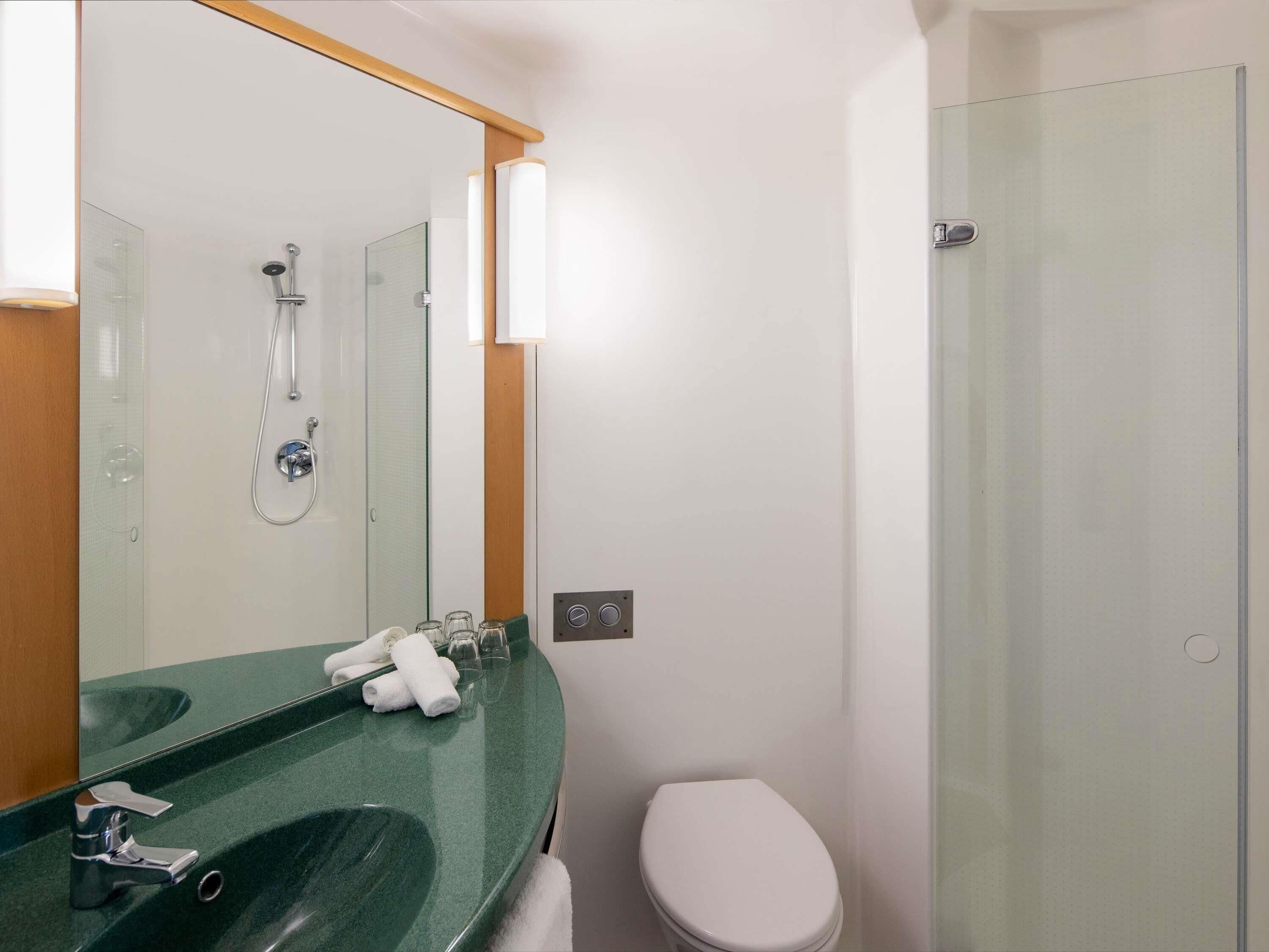 Une salle de bain moderne avec un lavabo vert, une douche en verre et des toilettes blanches.