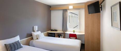 Una habitación de hotel con dos camas, un escritorio con silla, un televisor y una ventana con cortinas.