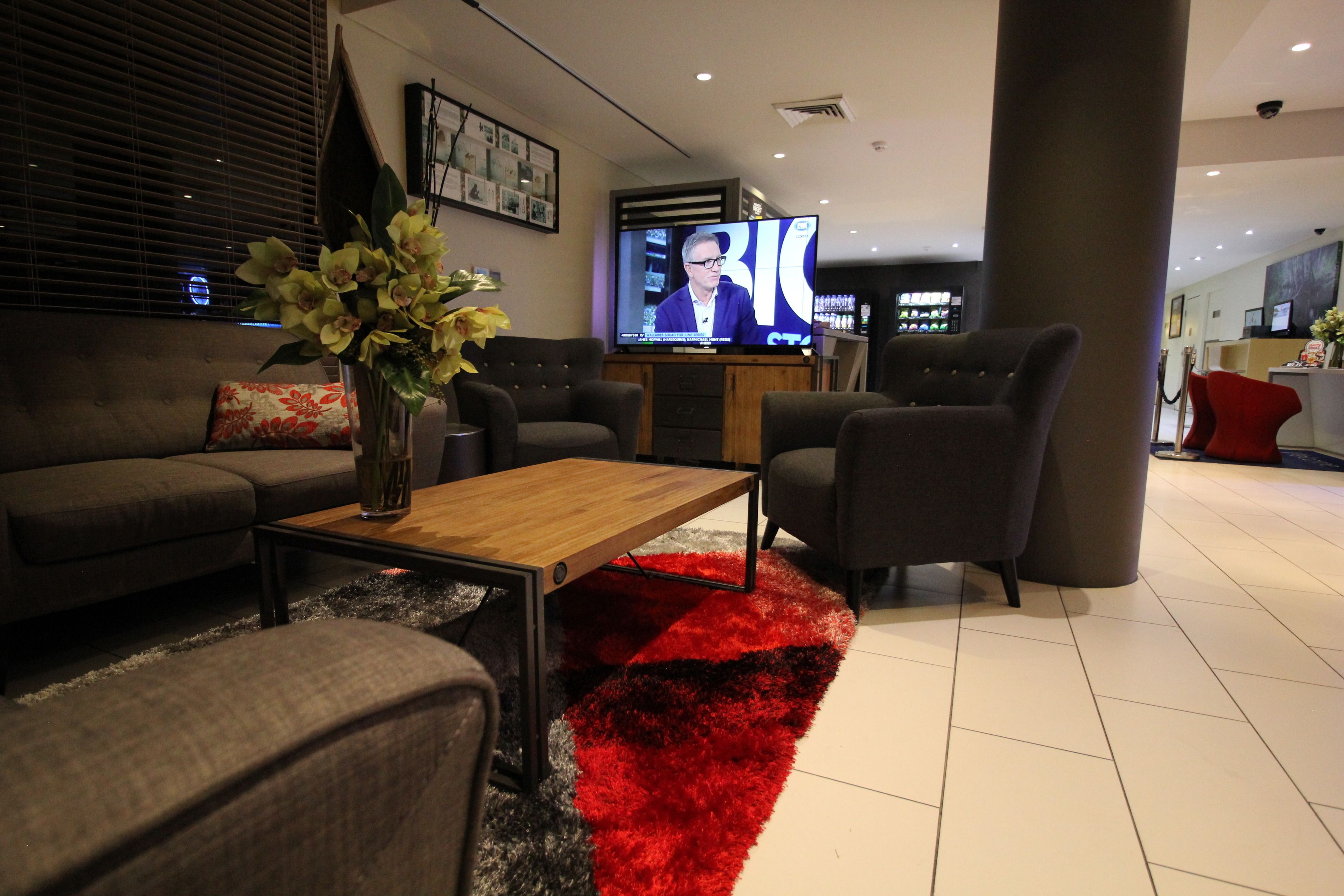 A modern living room with a sofa, armchairs, a coffee table, and a TV displaying a news program.