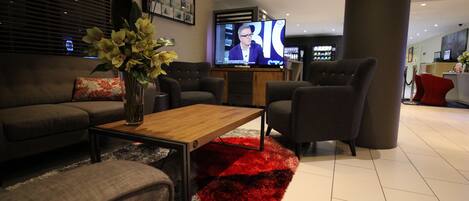 A modern living room with a sofa, armchairs, a coffee table, and a TV displaying a news program.