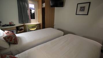 A hotel room with two beds, a desk, a chair, a TV mounted on the wall, and a window with curtains.