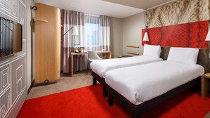 Una habitación de hotel con una cama grande, un escritorio con una silla, un televisor y una alfombra roja.