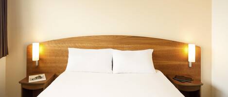 A hotel room with a large bed, two bedside tables, and wall-mounted lights.