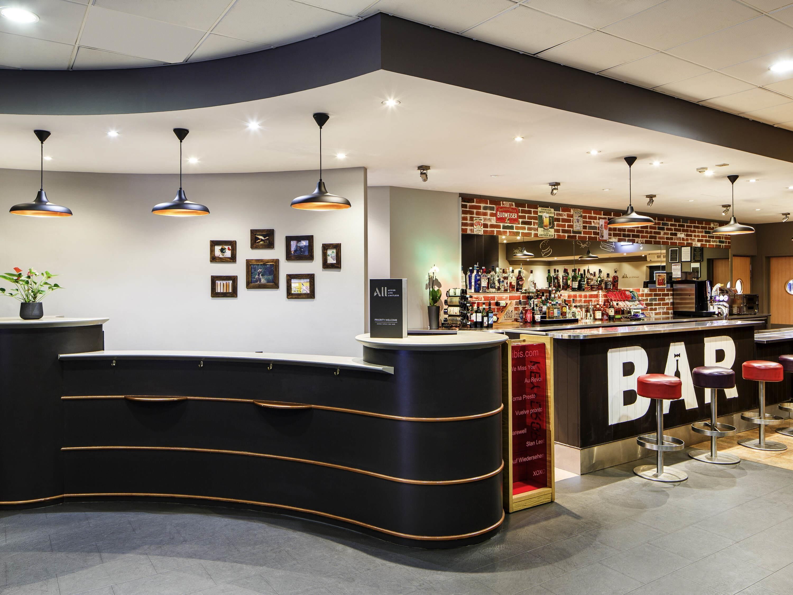 A modern bar area with a curved reception desk, multiple hanging pendant lights, and a well-stocked bar counter.