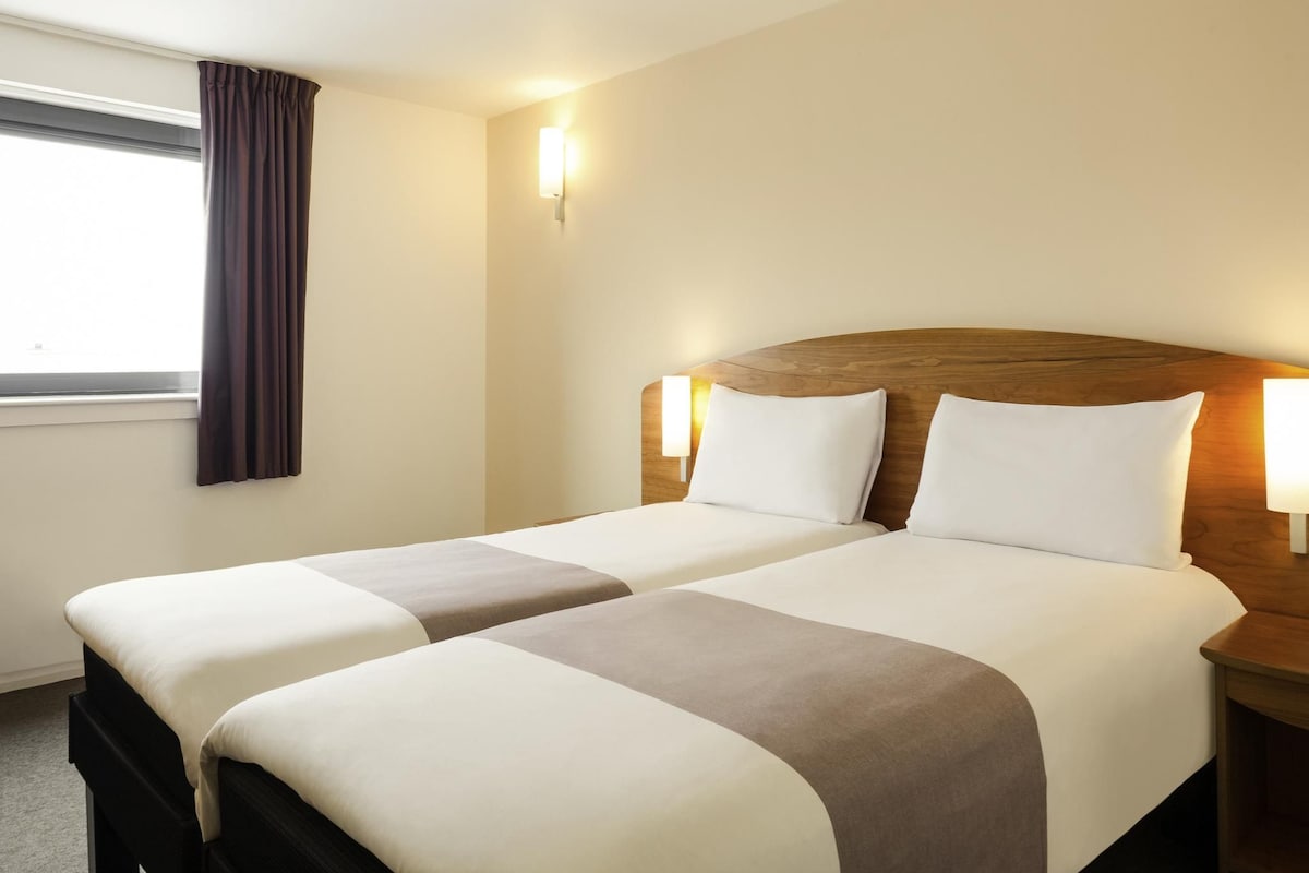 Habitación de hotel con dos camas, una ventana con cortinas y lámparas de noche.