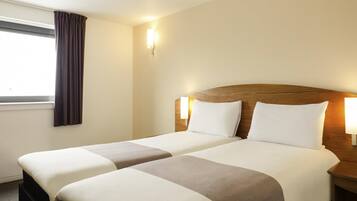 A hotel room with two beds, a window with curtains, and wall-mounted lamps.