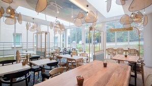 A spacious indoor dining area with multiple tables and chairs, large windows offering views of the outdoors, and hanging pendant lights with a woven design. - ibis Styles Pontivy Centre Bretagne (Pontivy)