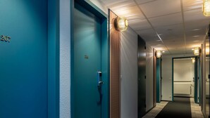 A hallway with teal-colored doors numbered 206 and 207, a textured wall, and a carpeted floor. - ibis Styles Pontivy Centre Bretagne (Pontivy)